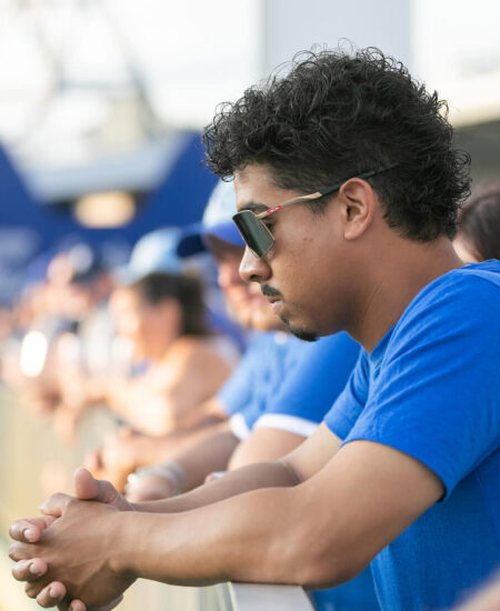 Man in blue shirt and sunglasses leans on railing outdoors.