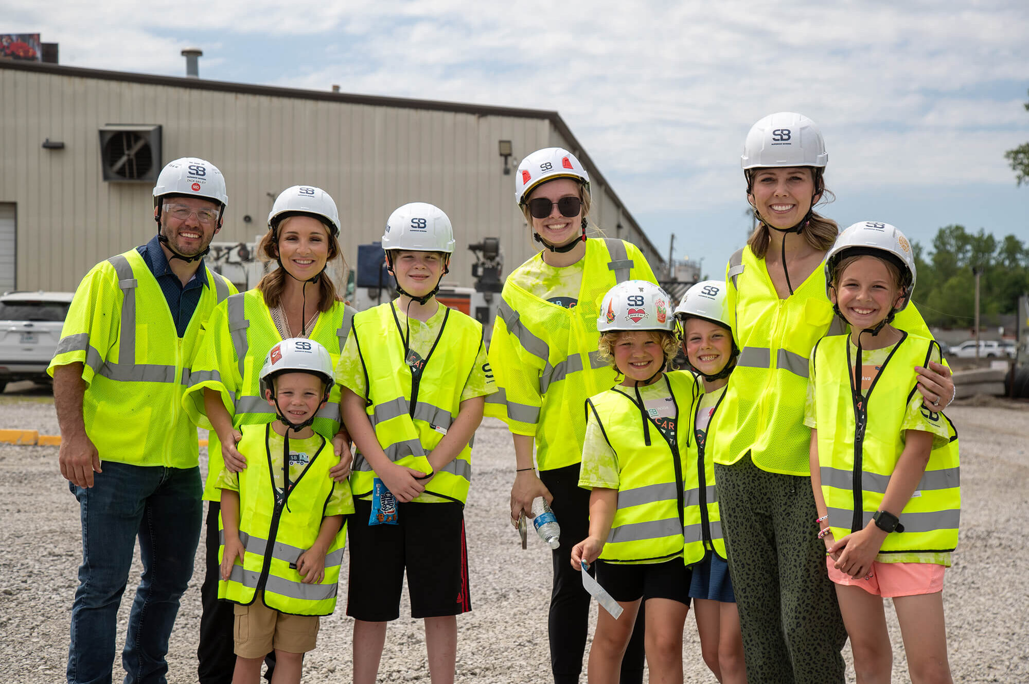 Adults and children in safety vests and hard hats outside.
