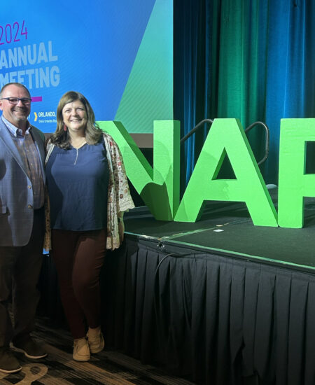 Two people smile by large green NAP letters on stage.