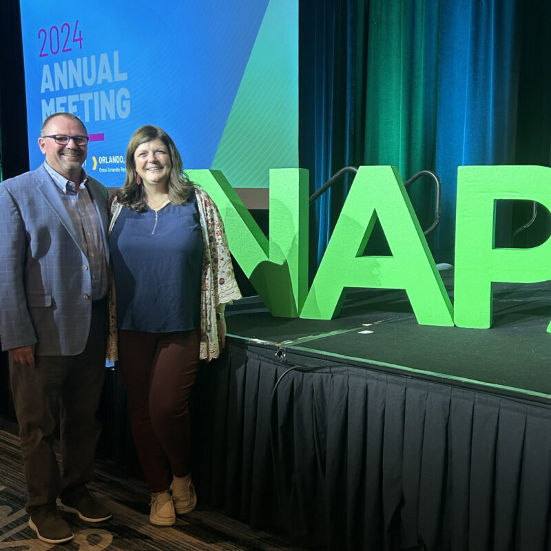 Two people smile by large green NAP letters on stage.